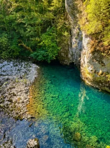 A view from above of the crystal-clear, emerald-turquoise water at the very source of the Bastašica River, with the stone bottom clearly visible beneath steep, moss-covered cliffs