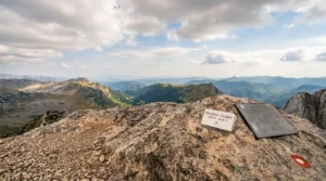 Rocky summit of Zelena Glava with a prominent hiking sign and elevation marker, overlooking the vast mountain landscape of Bosnia and Herzegovina