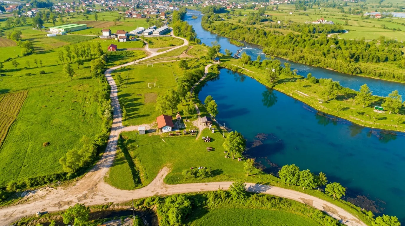 An aerial view showing the blue Mrkotić Lake surrounded by rich green meadows, trees, and country roads