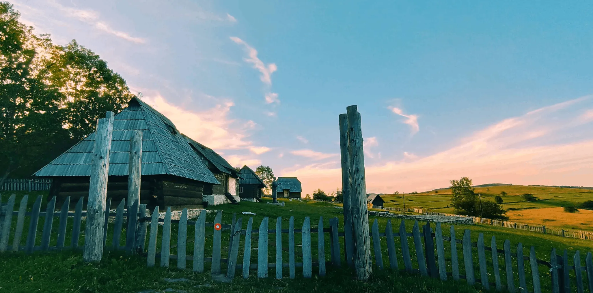 Traditional wooden structures and a fence on Manjača at sunset