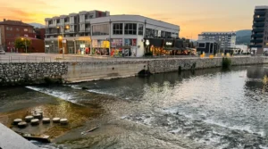 Kiseljak merkezindeki taş kıyı ve binalarla birlikte Lepenica Nehri’nin akışına bakış; gün batımı sırasında erken akşam gökyüzünün sıcak tonlarıyla aydınlanmış