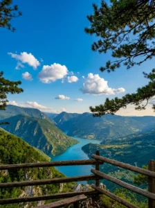 Vista panoramica spettacolare da un belvedere in legno sul magnifico intreccio e meandro del fiume Tara azzurro, che serpeggia sul fondo di un profondo canyon sotto il cielo sereno e le nuvole bianche