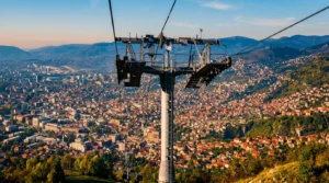 Sarajevo teleferiğinin direk yapısının yakın plan görüntüsü, arka planda gün batımı sırasında Sarajevo’nun görkemli panoraması