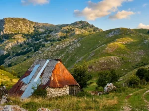Stara, avtentična pastirska koča s kamnitimi zidovi in zarjavelim pločevinastim strešnim kritjem na zelenih, hribovitih pobočjih vasi Umoljani na Bjelašnici