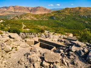 Pogled sa visine na masivne betonske ukopane jarke i zidine razrušene austrougarske tvrđave Strač, okružene hercegovačkim kršem i brdima pod plavim nebom