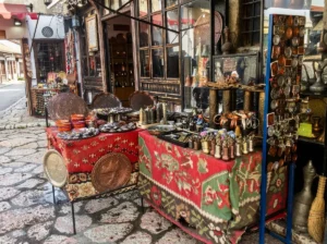 Close-up of stalls covered with red tablecloths with traditional patterns, displaying hand-forged souvenirs, džezvas, and fildžans in Kazandžiluk