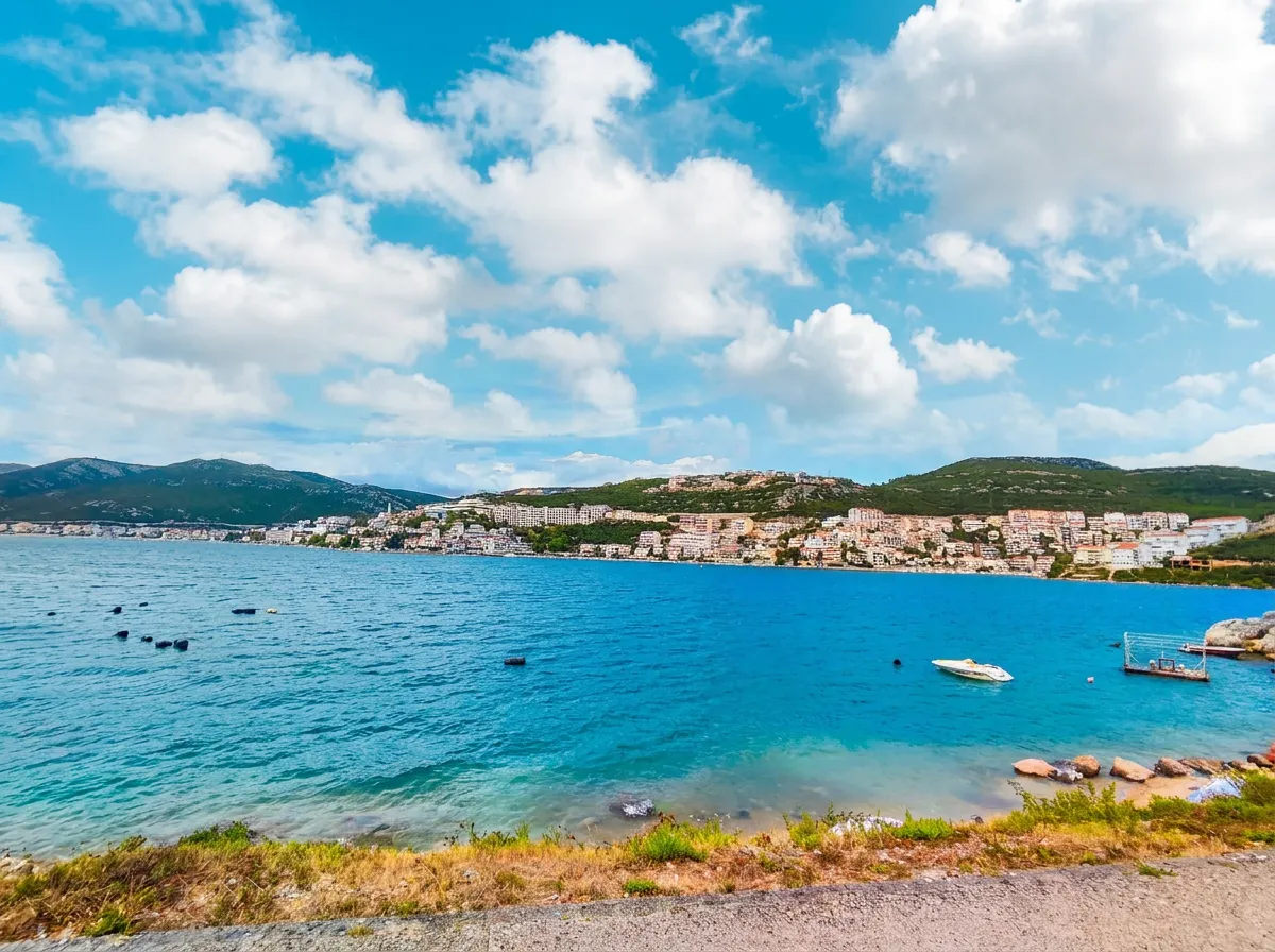Wide view of the blue Neum Bay and densely built hotels along the hillside under a striking blue sky with dynamic white clouds